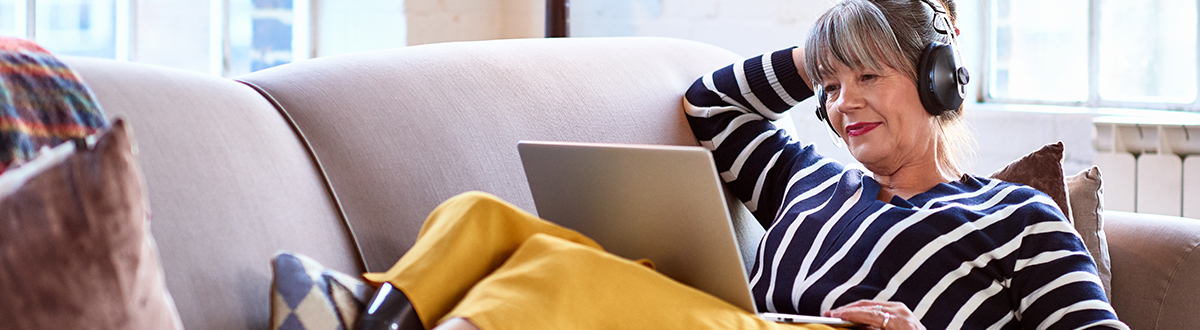 Seorang wanita bersantai di sofa dan mendengarkan musik melalui laptop